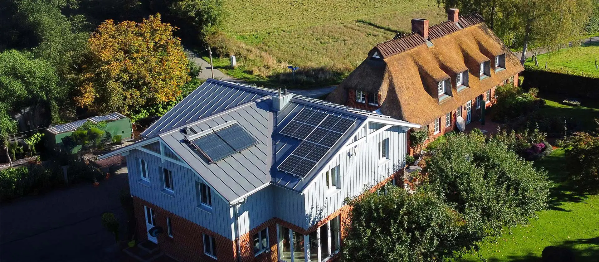 Ein Landhaus in Flensburg mit einem Reetdach, daneben ein modernes Haus mit Photovoltaikanlage