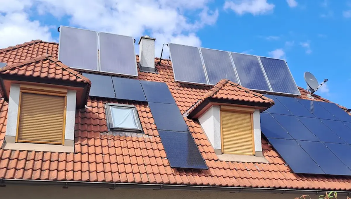 Ein rotes Hausdach mit zwei herausragenden Fenster und einigen Solarmodulen.