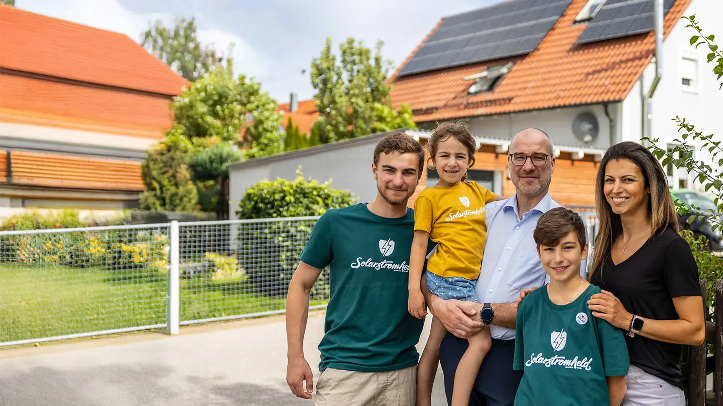 Eine Familie steht glücklich vor einem Haus mit einer Photovoltaikanlage auf dem Dach