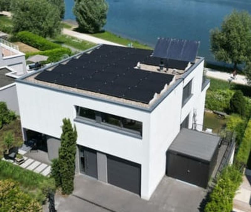 Eine aufgeständerte Photovoltaikanlage auf einem weißen Haus mit Flachdach.