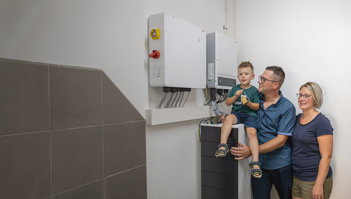 Eine Familie mit Kleinkind steht vor einem Stromspeicher für eine Photovoltaikanlage