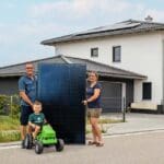 Familie steht vor einem Haus und hält ein Solarmodul in der Hand